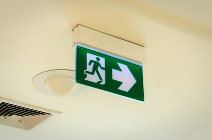 green emergency fire exit sign on ceiling in office building or ...